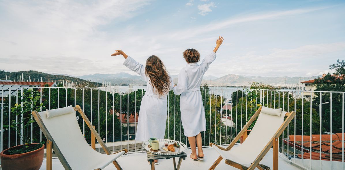 Zwei Frauen genießen den Ausblick von ihrem Hotel-Balkon auf einen Hafen