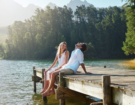 Paar sitzt im Sommer auf einem Steg am See und lacht vor Freude