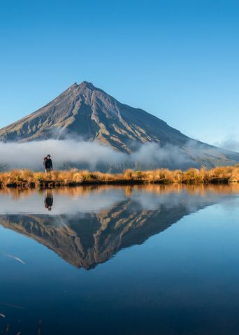 Der Mount Taranaki spiegelt sich mit seiner markanten Spitze in einem stillen See in Neuseeland.