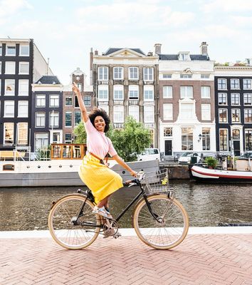 Frau fährt mit dem Fahrrad entlang einer Gracht in Amsterdam