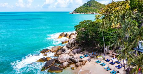Blick auf felsige Küste von Koh Phangan mit Liegen, Palmen und klarem Wasser