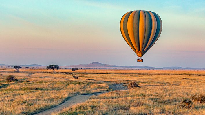 Heißluftballon fliegt bei Sonnenaufgang über den Serengeti Nationalpark in Tansania