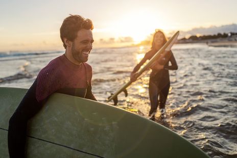 Zwei Surfer laufen mit Brettern bei Sonnenuntergang durch die Wellen am Strand