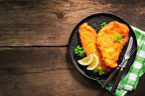 Goldbraune Wiener Schnitzel werden mit Pommes frites, Zitrone und frischen Kräutern serviert