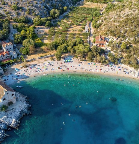 Luftaufnahme der Bucht Dubovica auf der Insel Hvar in Kroatien mit Kiesstrand, Steinhäusern und klarem Wasser