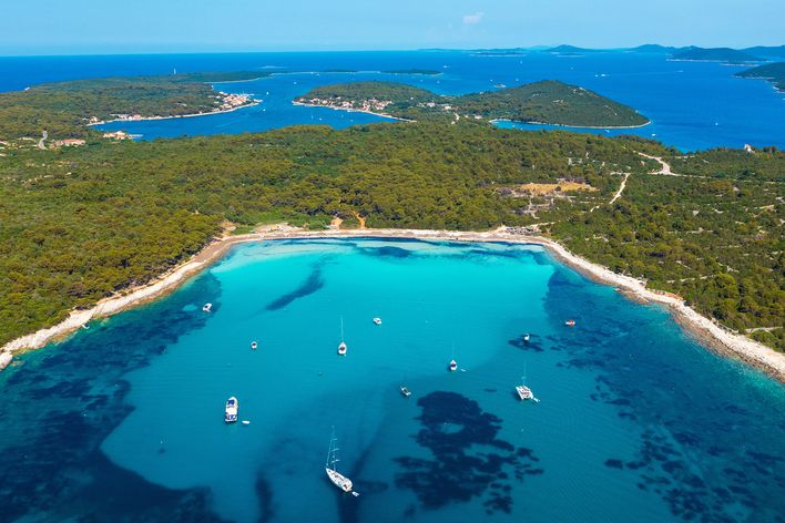 Luftaufnahme des Sakarun-Strandes auf der Insel Dugi Otok in Kroatien mit türkisfarbenem Wasser, Pinienwald und Booten