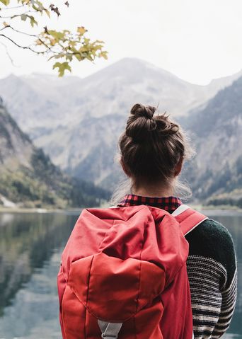 Blick auf die Rückansicht einer Frau mit Rucksack, die vor einem Bergsee auf die Berge blickt