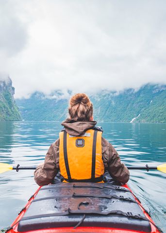 Frau paddelt im Kajak über Bergsee mit klarer Spiegelung der Gipfel