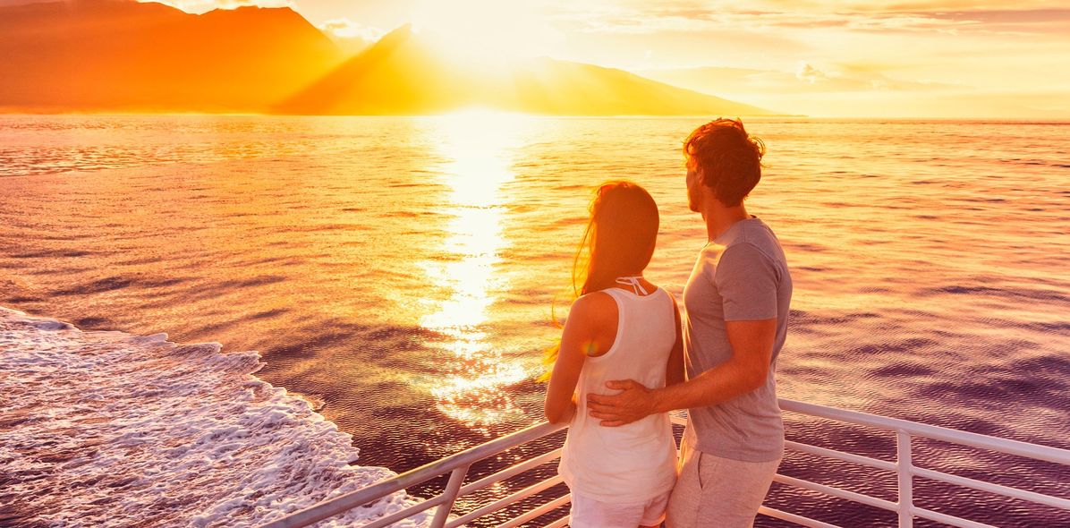 Paar an der Reling eine Kreuzfahrtschiffes vorm Sonnenuntergang