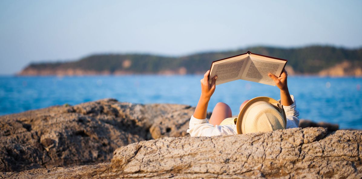 Frau auf einem Felsen buchlesend am Meer