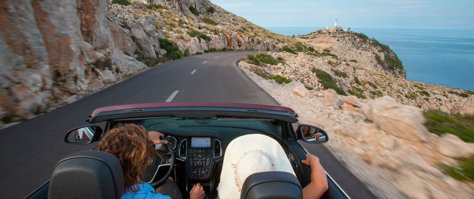 Personen fahren im Cabrio am Cap de Formentor eine Küstenstraße entlang, Blick aufs Meer