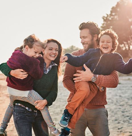 Eltern mit Kindern im Arm laufen fröhlich im Herbst am Strand entlang
