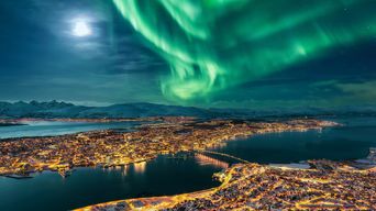 Blick auf die verschneite Stadt Tromso von oben bei Nacht und Nordlichter am Himmel, Norwegen
