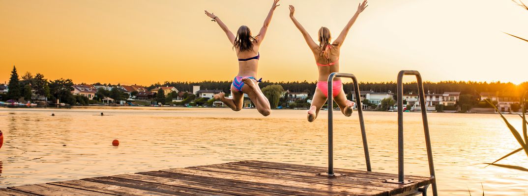 Zwei Frauen  die bei Sonnenuntergang in einen Badesee springen