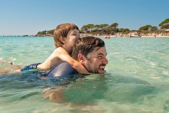 Vater trägt lachend seinen Sohn auf den Schultern im Meer bei Sonnenschein