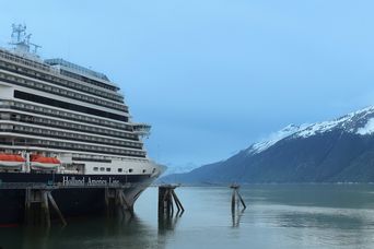 Ein Schiff der Holland America Line liegt an einem Anleger vor schneebedeckten Bergen in Alaska.
