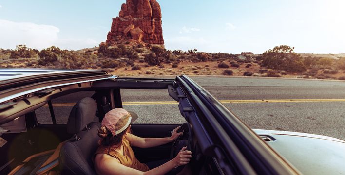 Frau im Cabrio vor roter Felslandschaft im Arches Nationalpark in den USA