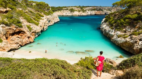 Frau blickt auf die Badebucht Calo des Moro mit türkisfarbenem Wasser und Felsen