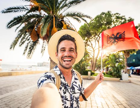  Ein Mann lächelt in Kamera und hält eine albanische Flagge in der Hand