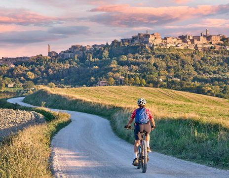 Frau fährt mit einem Fahrrad auf einem Feldweg in Monteriggioni in der Toskana