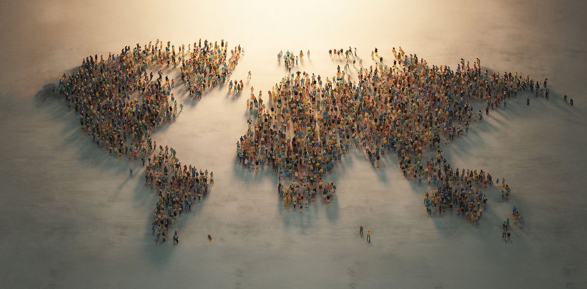Eine vielfältige Menschenmenge bildet die Form einer Weltkarte, die alle eine zentrale Lichtquelle anblickt