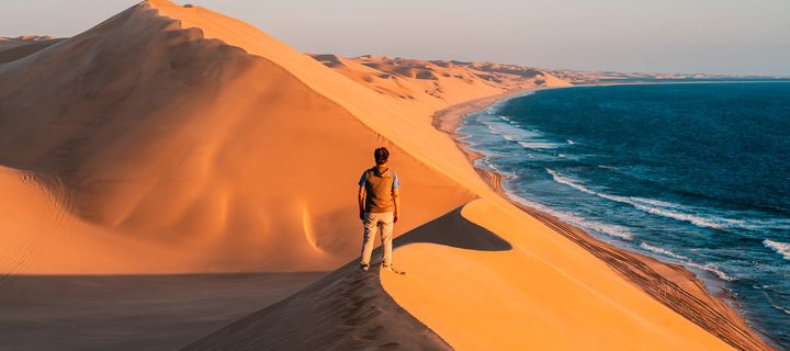 Reisende erklimmen die leuchtend orangefarbenen Dünen bei Walvis Bay in Namibia