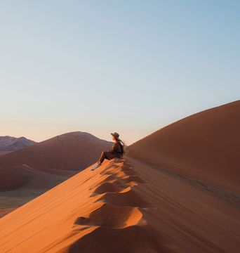 Frau sitzt in der Wüste im Namib Naukluft Nationalpark in Namibia und genießt den Ausblick