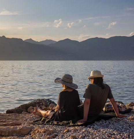 Paar sitzt am Ufer des Gardasees und genießt den Sonnenuntergang mit Blick auf die Berge