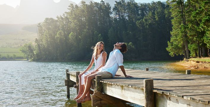 Paar sitzt im Sommer auf einem Steg am See und lacht vor Freude