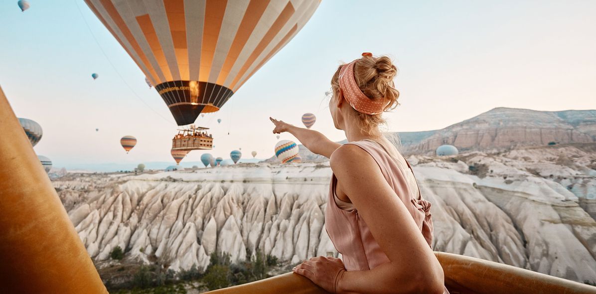 Frau sitzt auf einer Terrasse in Kappadokien, während Heißluftballons in den Himmel steigen