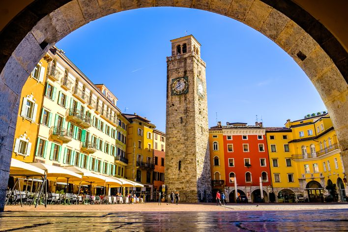 Blick durch einen Torbogen auf den Torre Apponale und bunte Häuser in der Altstadt von Riva del Garda am Gardasee