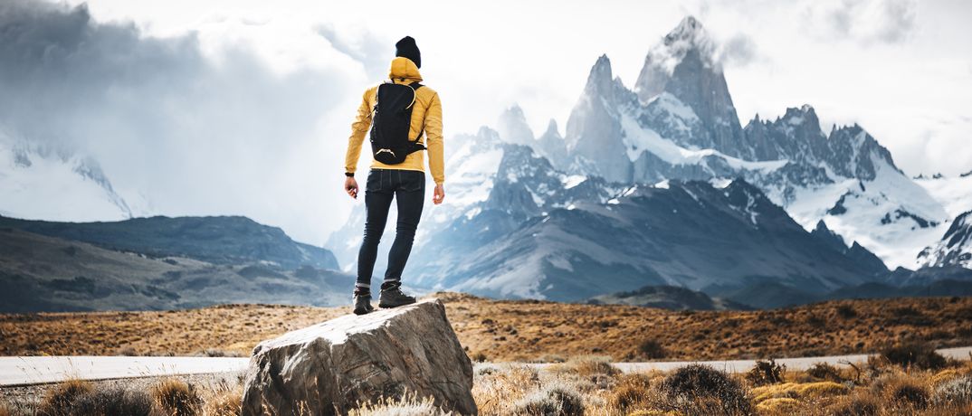 Reisender steht auf Felsen mit Blick auf die imposanten Gipfel des Fitz Roy in Patagonien, Argentinien