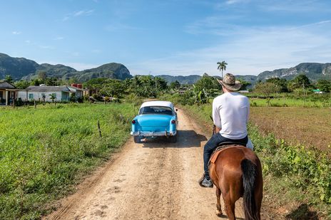 Mann mit Hut auf einem Pferd reitet hinter einem Oldtimer im Vinales-Tal auf Kuba
