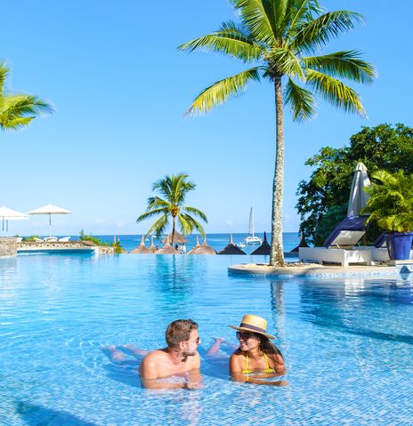Paar entspannt im Pool eines Hotels auf Mauritius mit Palmen und Meerblick