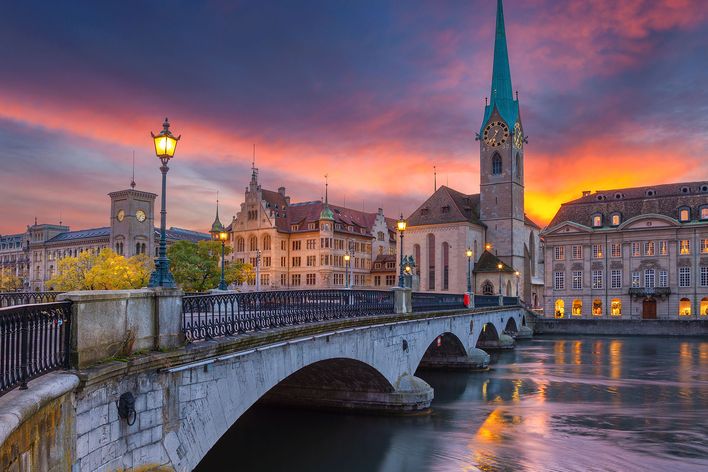 Zürichs Altstadt und die Limmat leuchten bei einem farbenprächtigen Sonnenuntergang rund um die Münsterbrücke.