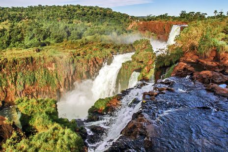 Panoramablick auf die Iguazú-Wasserfälle mit rotem Fels und tropischem Grün