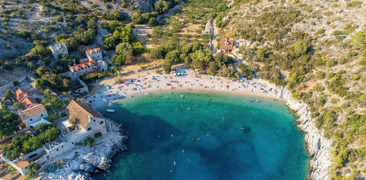 Luftaufnahme der Bucht Dubovica auf der Insel Hvar in Kroatien mit Kiesstrand, Steinhäusern und klarem Wasser