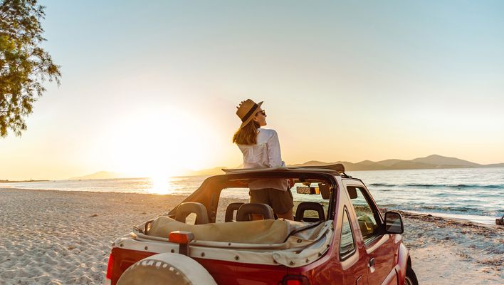 Frau am Strand mit einem Mietwagen
