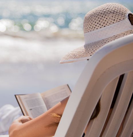 Frau liest Buch auf einem Liegestuhl am Strand