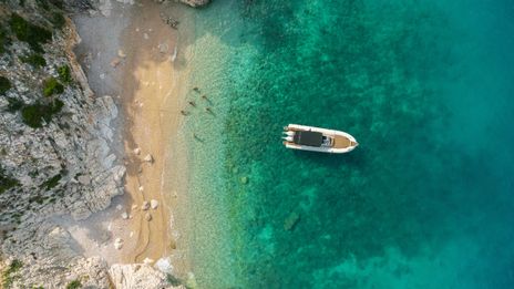 Luftaufnahme von einem Boot am Strand von Kroatien mit Menschen im Wasser