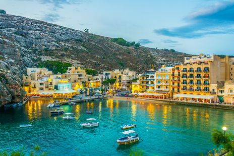 Die Stadt Xlendi auf der Insel Gozo in der Abenddämmerung mit beleuchteter Promenade und kleinem Hafen, Malta