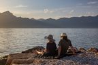 Paar sitzt am Ufer des Gardasees und genießt den Sonnenuntergang mit Blick auf die Berge