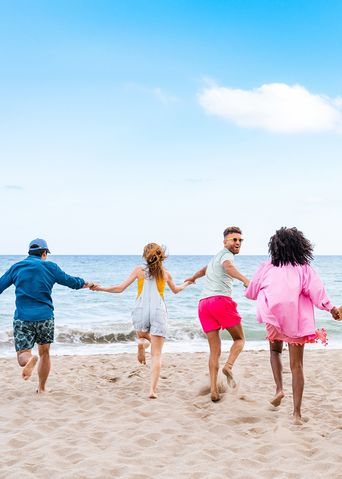 Gruppe junger Leute läuft Hand in Hand am Strand Richtung Meer
