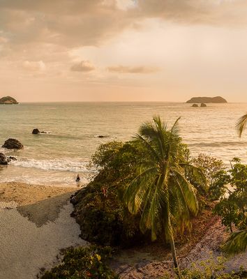 Tropischer Strand in Costa Rica bei Sonnenuntergang mit Palmen und Felsen am Wasser