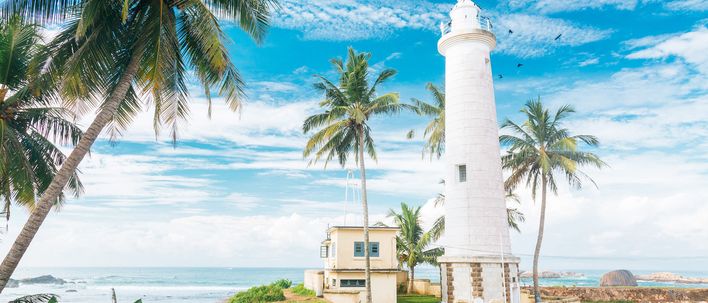 Weißer Leuchtturm im historischen Galle Fort an der Südküste Sri Lankas, umgeben von Palmen und blauem Himmel