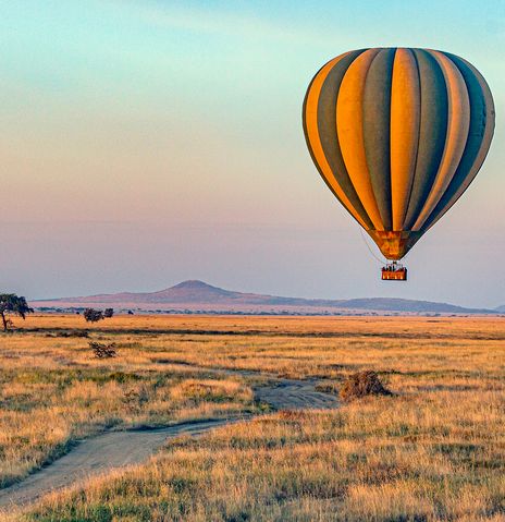 Heißluftballon fliegt bei Sonnenaufgang über den Serengeti Nationalpark in Tansania