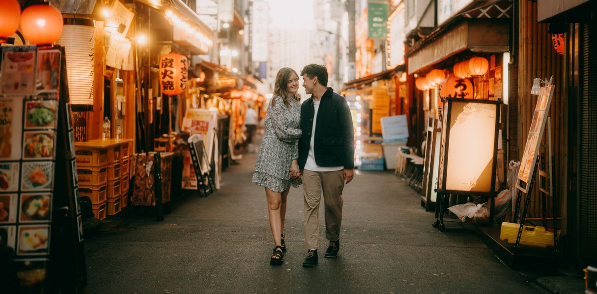 Fröhliches junges Paar, das durch eine Gasse in Tokio läuft