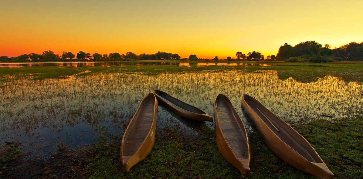 Drei Einbaumboote liegen an einem Ufer des Okawango-Deltas während des Sonnenuntergangs in Botswana