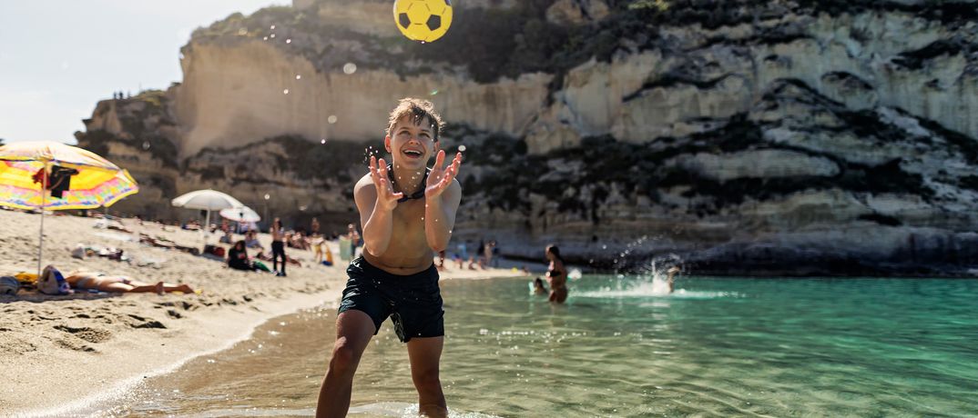 Kind spielt mit einem Ball im klaren türkisfarbenen Meer an einem Sandstrand in Tropea in Kalabrien
