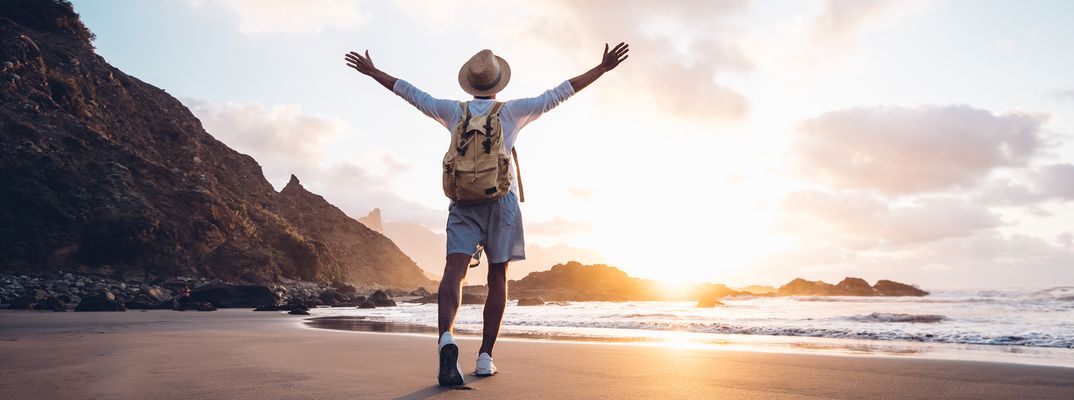 Mann breitet am Strand die Arme aus und genießt den Sonnenuntergang am Meer